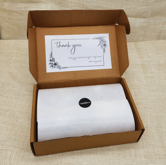 Open cardboard box with a white sheet of paper and a 'thank you' card on a beige fabric background
